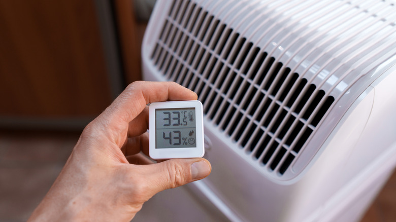 close up of a hand holding a thermostat in front of a portable air conditioner
