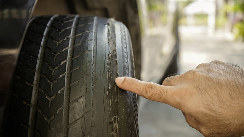 Close up of a man's finger pointing at weared car tire tread