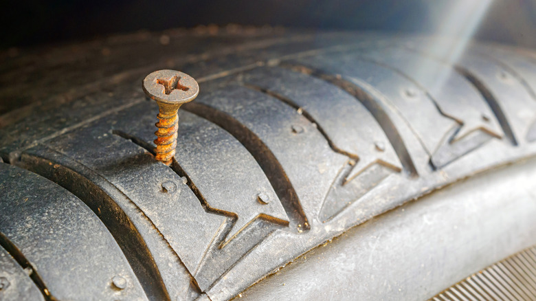A close-up of a rusty screw lodged in a tire surface.
