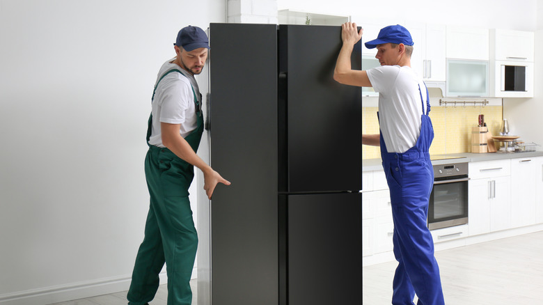 Movers moving a fridge in a kitchen.