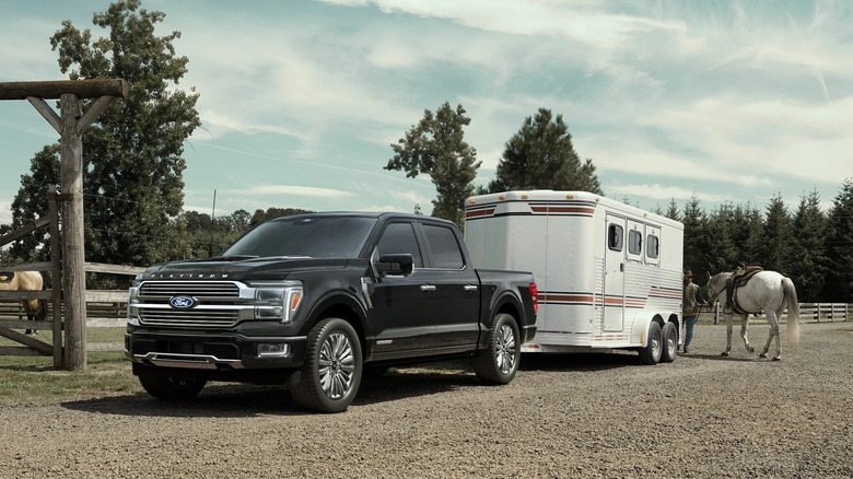 Ford F-150 PowerBoost hybrid with livestock trailer and horse in background, front-left 3/4 view