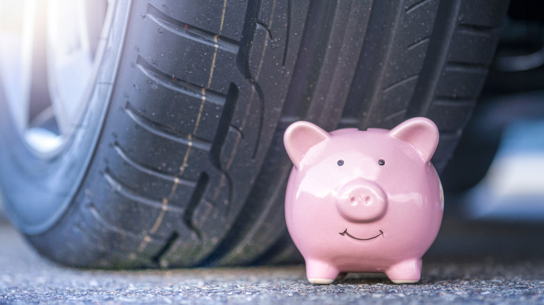 A close-up of a small pink piggybank placed next to a car tire.