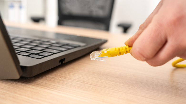 A person connecting an ethernet cable to a laptop placed on a wooden table