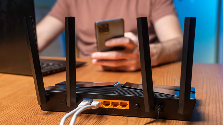A person using a smartphone and laptop with a router placed in the front on a table