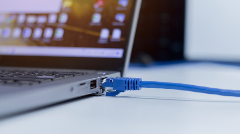 A blue LAN cable connected to a laptop placed on a white table
