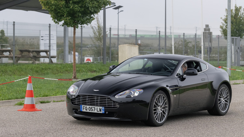 A black early 2010s Aston Martin Vantage parked at the side of a street.