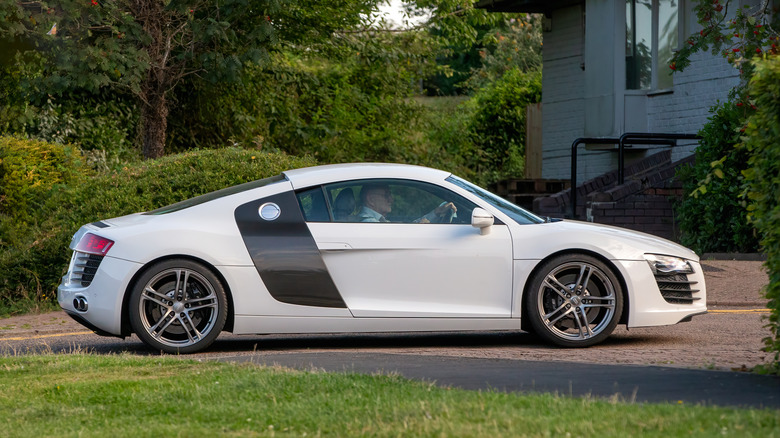 A white Audi R8 parked off a small road with foliage in the back.