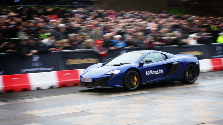 A blue McLaren MP4-12C supercar zooming down a quarter-mile strip.