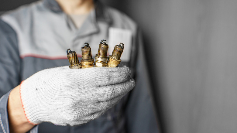 A mechanic holding four spark plugs in his gloved hand