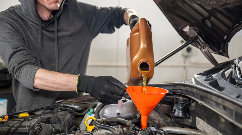 A mechanic pouring new oil into car with a funnel