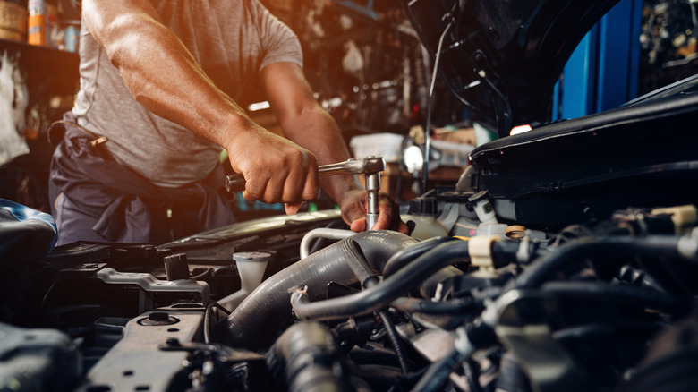 A mechanic turning a bolt on a car engine with a ratchet