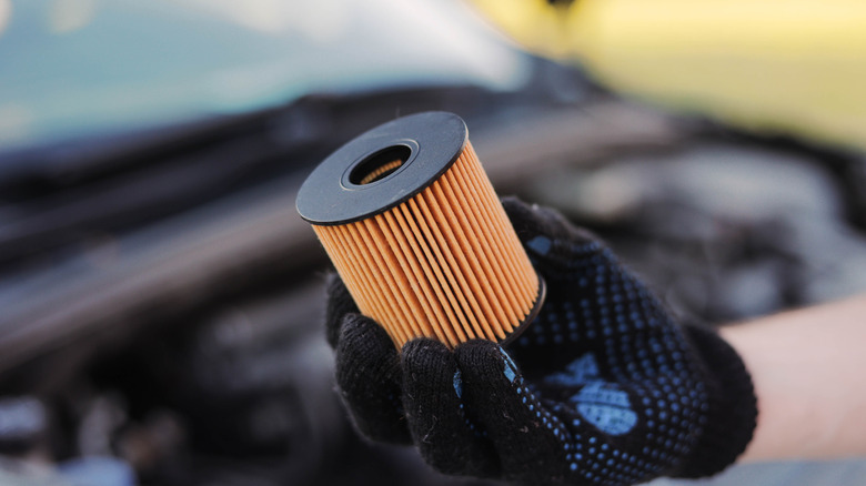 A mechanic wearing gloves holding an automotive oil filter