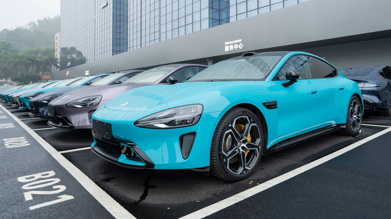 A row of Chinese Su7 electric vehicles parked outside a dealer on an overcast day