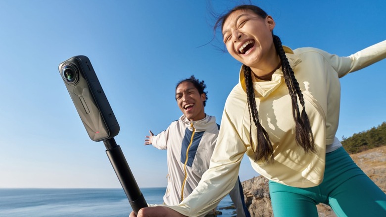 Two people using an Insta360 X5 camera on the beach.