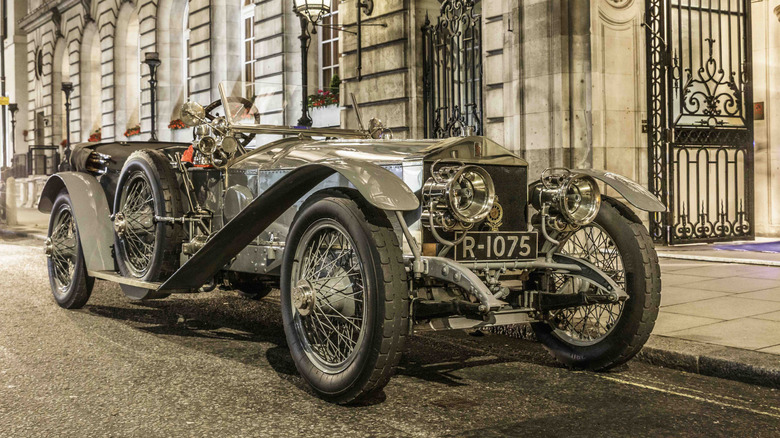 Vintage Rolls-Royce Silver Ghost seen from right front parked on street at night in front of an elegant building