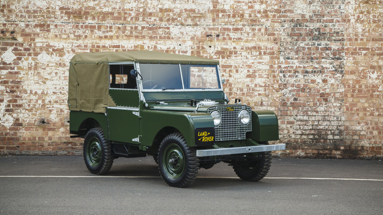 Vintage green Land Rover Series I seen from right front parked in front of a brick wall