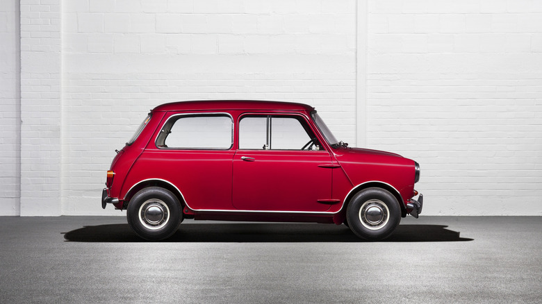 Red 1960 Morris Mini Minor seen from the right parked in front of a white brick wall
