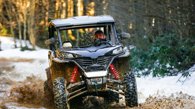 Man driving a four-wheeler over rough and snowy terrain.