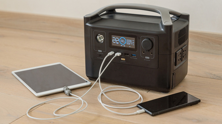 A portable power station on the floor charging a tablet and smartphone