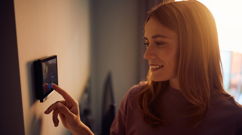 A woman using a smart home device on the wall.
