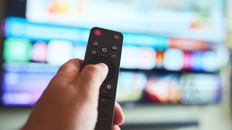 A person using a remote in front of a smart TV, blurred background.