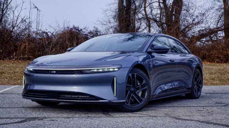 Gray Lucid Air in a parking lot with dried foliage in the background.