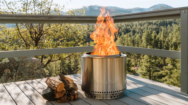 Solo Stove Bonfire 2.0 with a fire burning on a patio with forest in the background