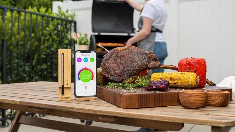 Meater Plus Bluetooth-Enabled Meat Thermometer, phone, and cutting board of food on table