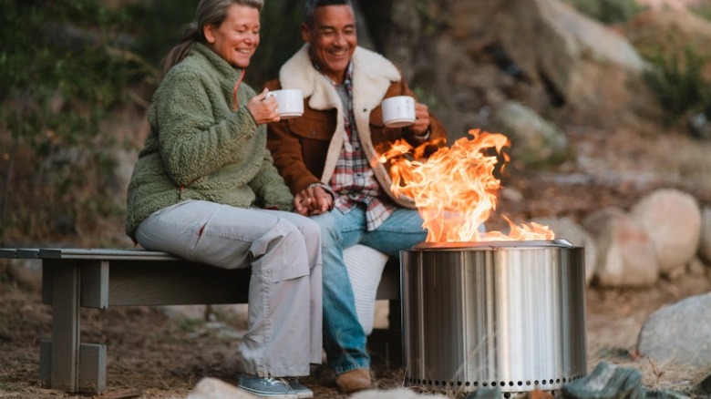 A man and a woman sitting on a bench in front of a Solo Stove Bonfire 2.0