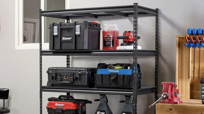 A heavy-dut black steel shelf inside a garage or storage space with multiple tools and cases