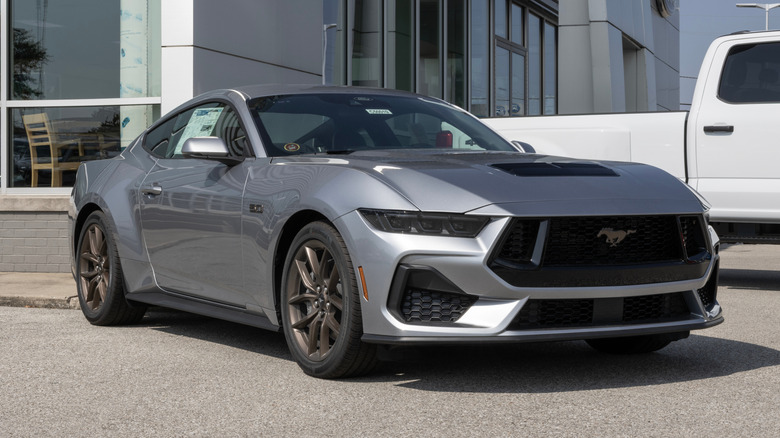 A brand new dark gray Ford Mustang GT Coupe parked in front of a dealership.