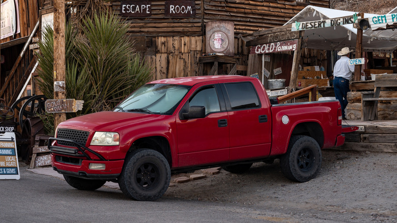 A 2000s red Ford F-150 parked in a "Wild-West town.