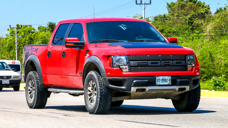 A red V8 Ford Raptor being driven on interurban roads with greenery in the background.