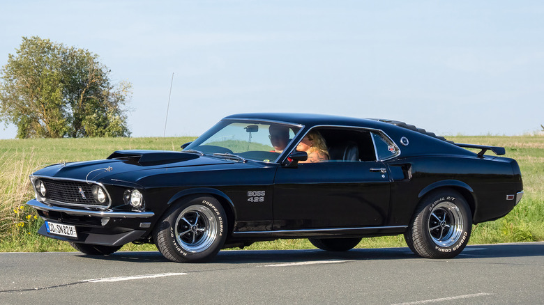 Two people driving a black Ford Mustang Boss 429 on a country road