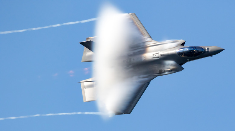 An F-35 flying fast, creating a vapor cloud around it