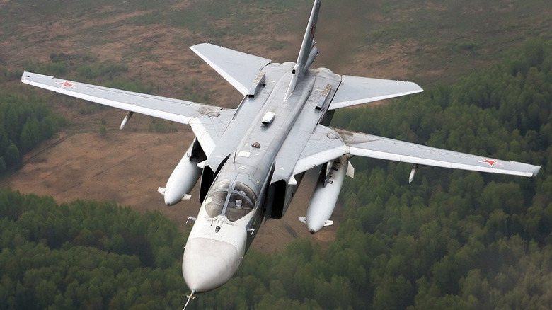 Sukhoi Su-24 aircraft flying over woodland terrain