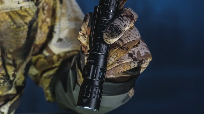 Close-up of a person in hunting gear holding a lit Coast TX300R flashlight