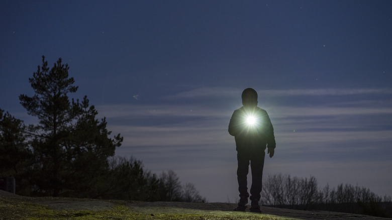 A person standing outdoors with a lit flashlight at dusk
