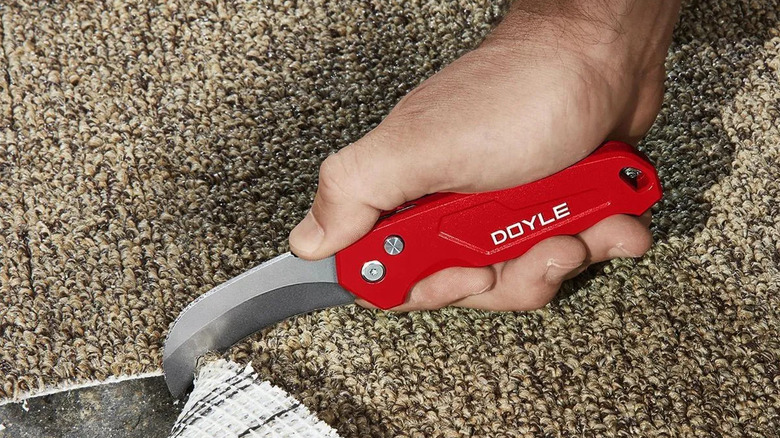 A red Doyle flip knife being used to cut carpet.