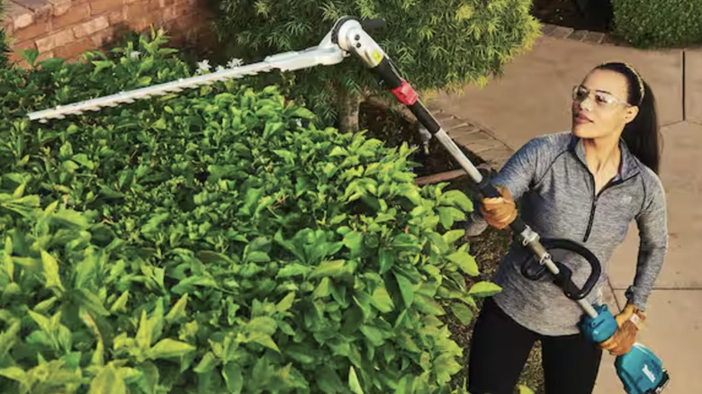A woman wearing safety glasses using the Makita Articulating Hedge Trimmer attachment