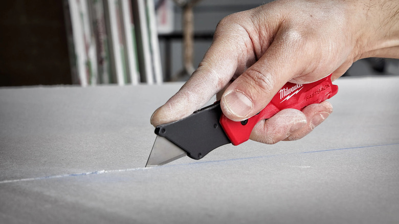 person using a Milwaukee Fastback Compact Folding Utility Knife to slice a surface