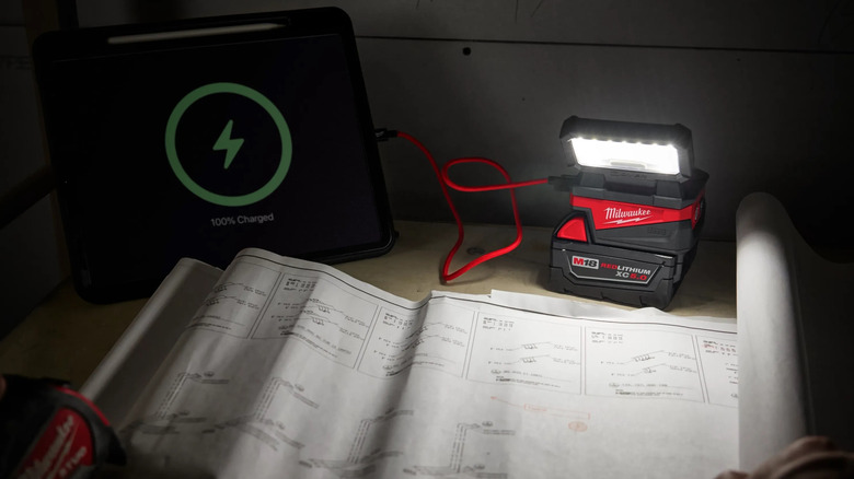 Milwaukee M18 Rover Compact Folding Flood Light plugged into a battery pack, illuminating work plans