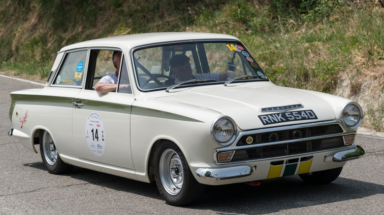 An Ermine White Ford Cortina Lotus with a driver and a passenger on a road