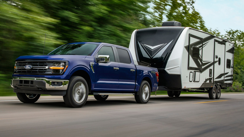 Front 3/4 view of blue Ford F-150 towing travel trailer down the road.