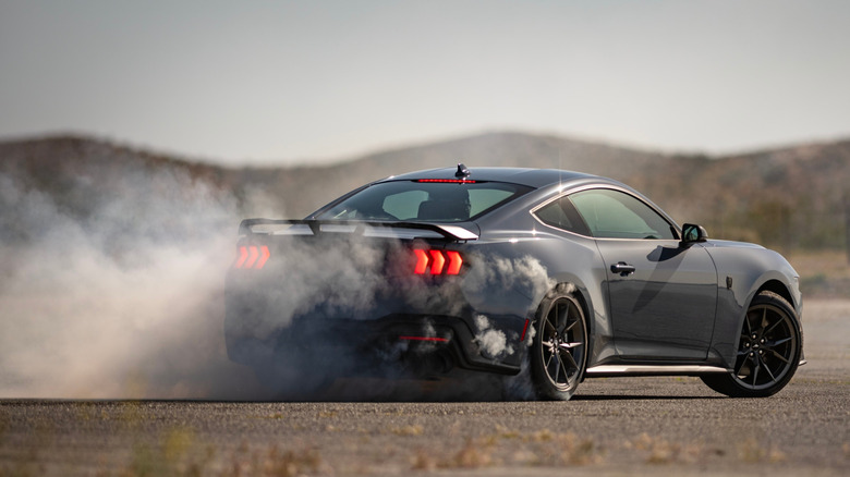 Rear view of Ford Mustang Dark Horse drifting on desert race track.