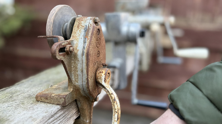Close-up of vintage hand-crank grinder clamped on wood