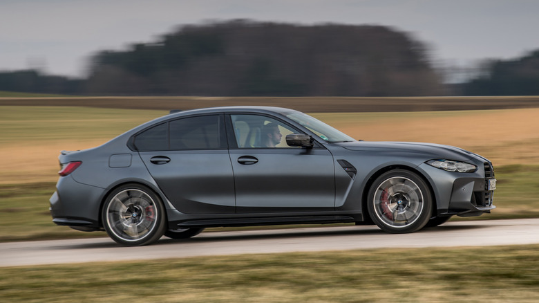 Side view of gray BMW M3 driving on country road.