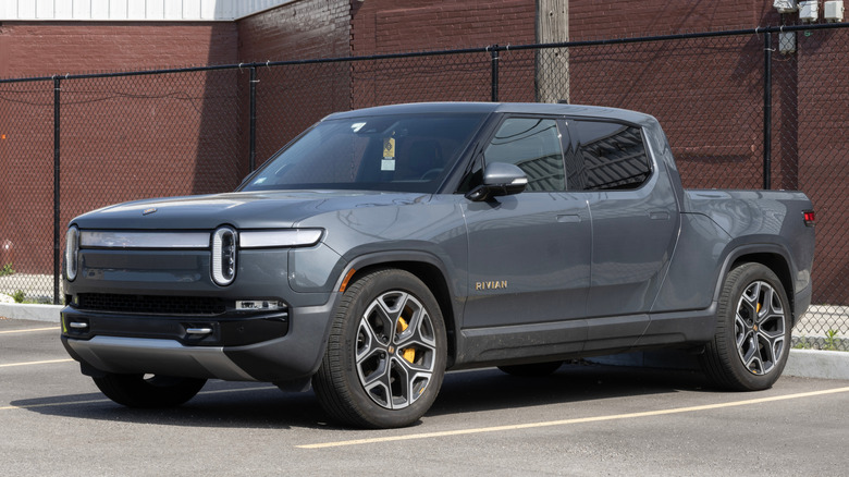 Front 3/4 view of gray Rivian R1T pickup parked in front of building.