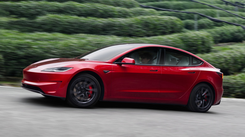 Side view of red Tesla Model 3 Performance driving on rural road.