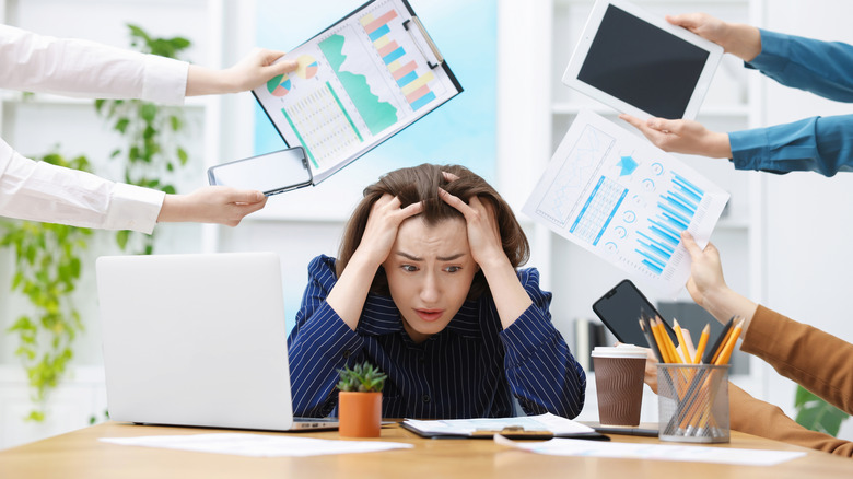 Overwhelmed woman sitting at laptop while colleagues hold other devices around her